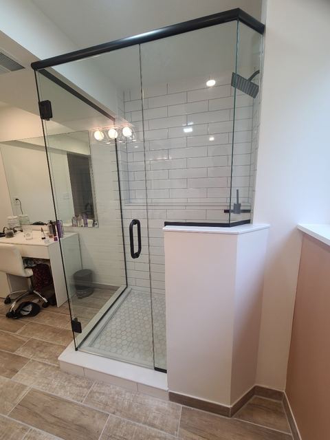 Frameless corner shower with black hardware on a half wall