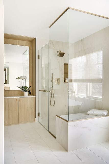 Frameless shower with a marble bench beside a recessed vanity mirror