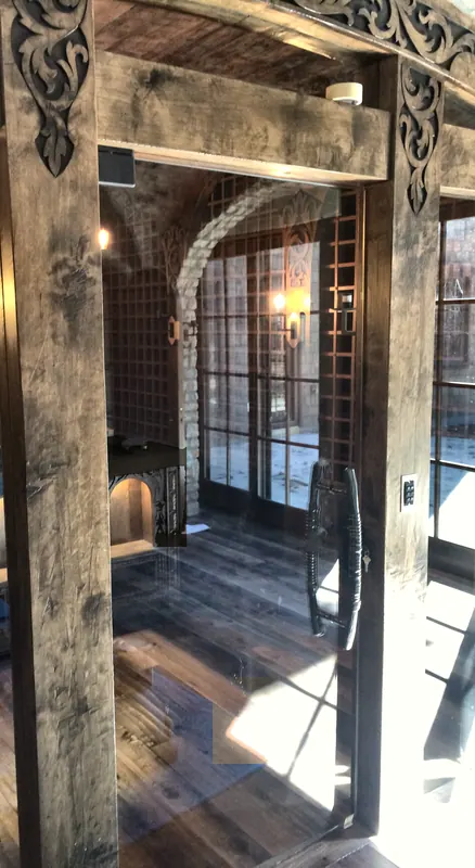 Glass door set into carved timber posts, opening onto a stone-arched wine cellar.