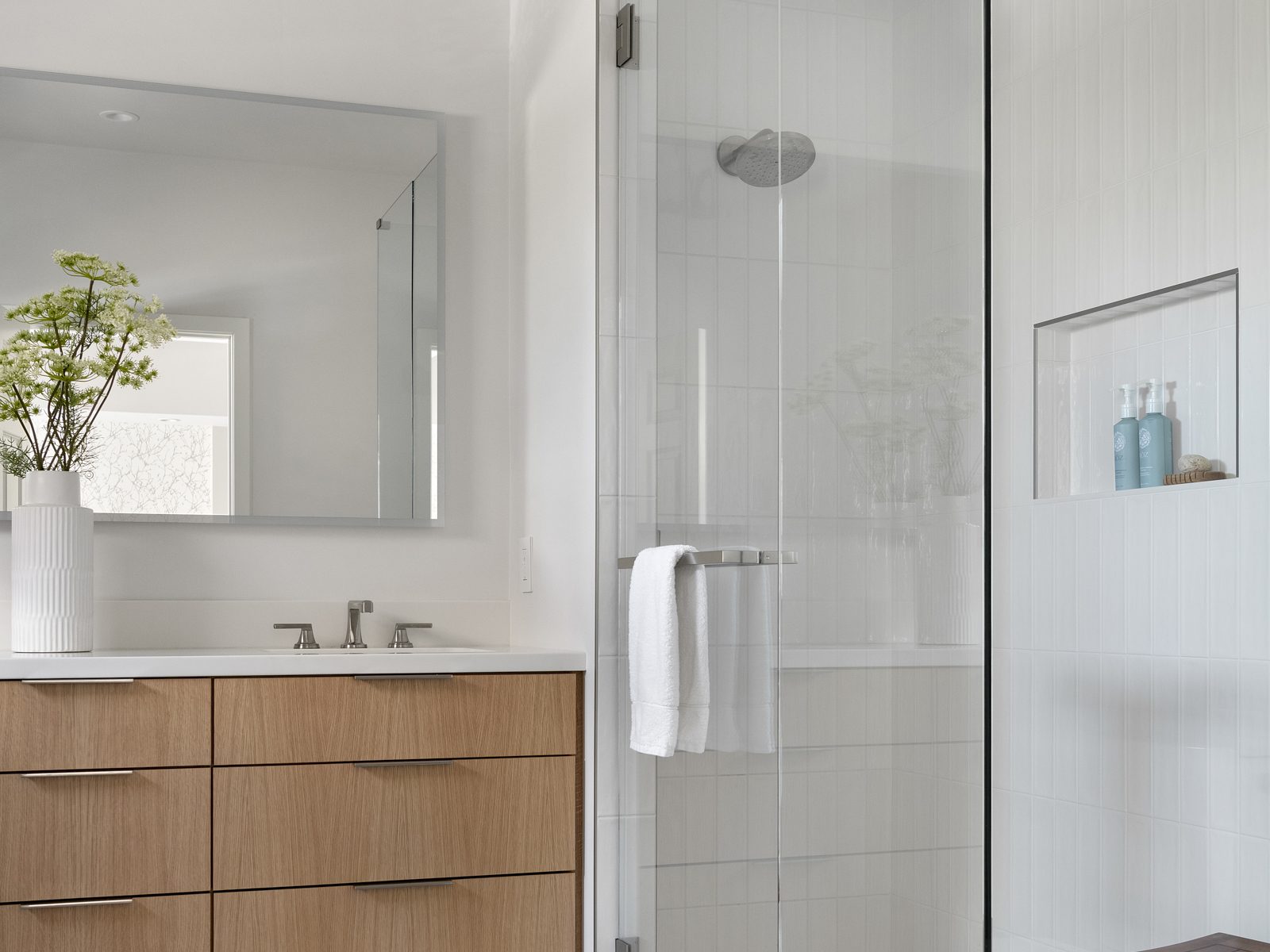 Frameless glass shower enclosure beside a wall-mounted custom vanity mirror